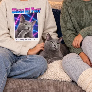90s Laser Portrait Cat Photo Sweatshirt styled in a lifestyle scene – two friends laughing on a dorm-style couch, one wearing the black sweatshirt, string lights on the wall, evening lamp light