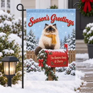 Santa Mailbox Cat Christmas Garden Flag styled in a lifestyle scene – the garden flag on its stand in a snowy front yard path beside a lantern-shaped solar light and a small evergreen shrub, soft overcast winter daylight